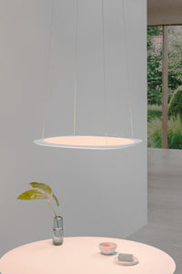 Flache Pendelleuchte Flying in weiß - stilvoll schwebend über rundem Tisch mit Vase und Schalen, vor minimalistischem Hintergrund